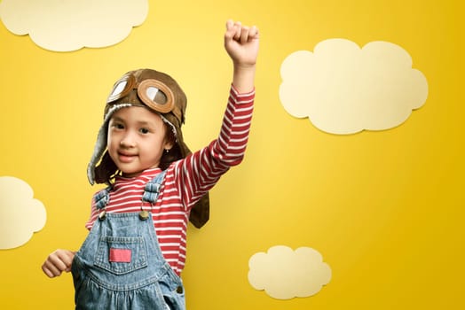 Cheerful asian kid with aviator hat and goggles having fun over yellow background