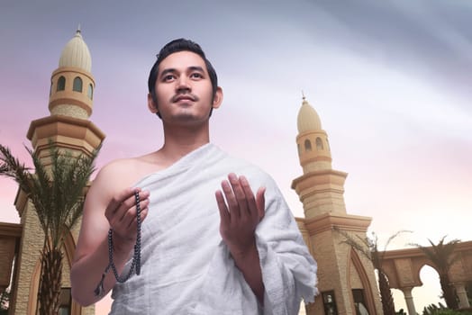 Young asian muslim man wearing ihram clothes with mosque background