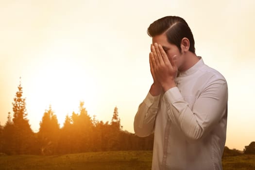 Asian muslim man with traditonal dress praying over sunset background
