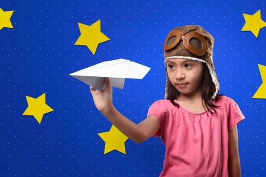 Cheerful asian kid with aviator hat playing paper planes on blue wall with star background