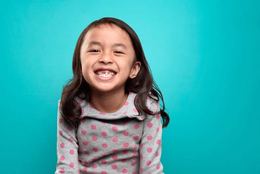 Smiling asian little girl and her broken teeth over blue background