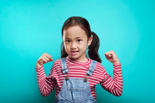 Happy asian kid showing her powerful hand over blue background