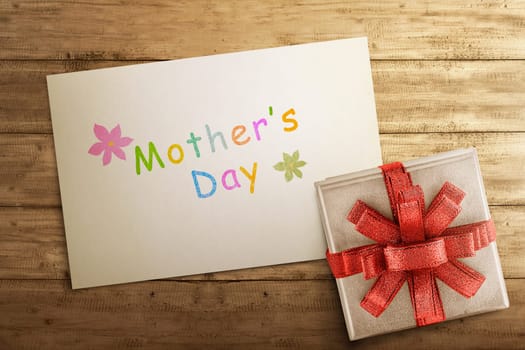 White gift box with Mother's day greeting on paper over wooden table