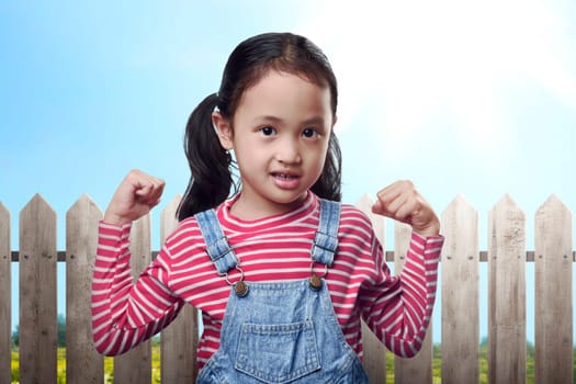Funny asian child showing muscle on her hand with park background