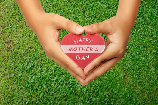 People hand holding heart with Happy Mothers day greeting on grass