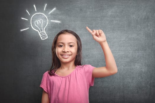 Cheerful asian kid with bright idea symbol above her head against blackboard background