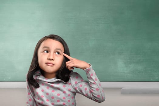Happy asian girl thinking with pensive expression against chalkboard background