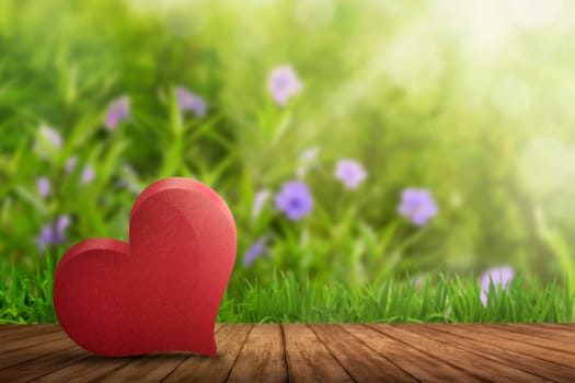 Red heart lying on wooden floor with garden background
