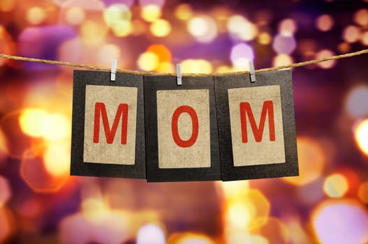 Mom word shape hanging with clothespin over blurred light background