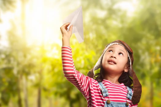 Cheerful asian child playing with paper plane on the park