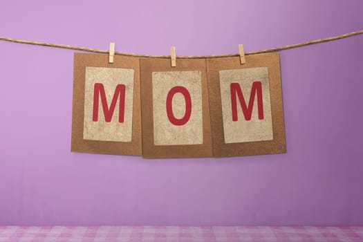Mom word shape hanging with clothespin against pink background