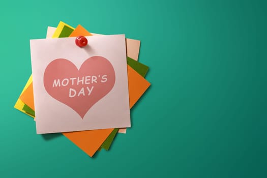 Mothers Day message written on stack of colorful paper note on green background