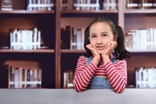Cheerful asian kid thinking for new idea in the library