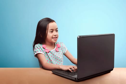 Smiling asian child with laptop computer on the table against blue background