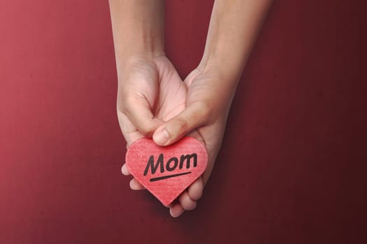 People hand holding red heart with Mother's Day message over red background