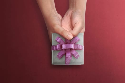 People hand holding small gift for Mother's Day over red background