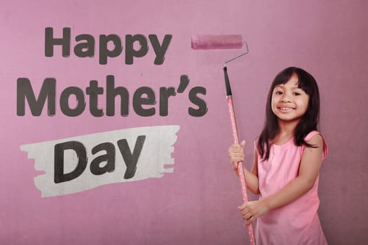 Happy asian little girl holding roller brush paint Happy Mothers day message over pink wall background