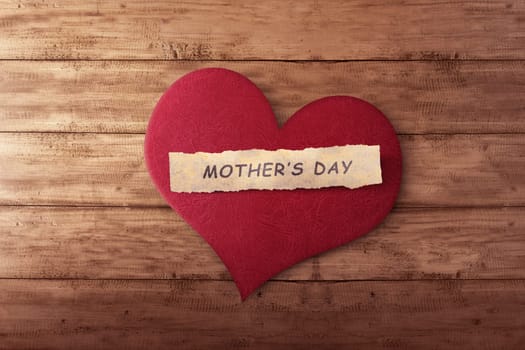 Mother's day message on ripped paper in red heart shape over timber background