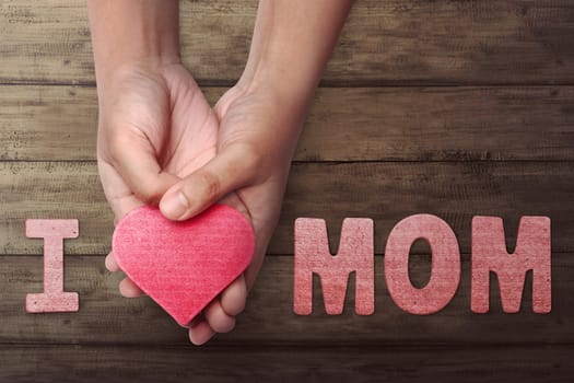 People hand holding red heart to make Mother's Day greeting in wooden table