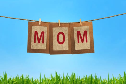 Mom word shape hanging with clothespin on blue sky background
