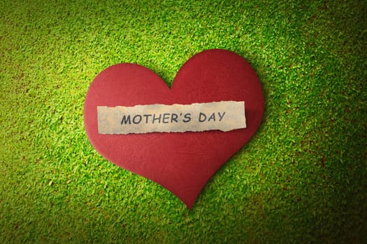 Mothers day message on paper in red heart over green grass background