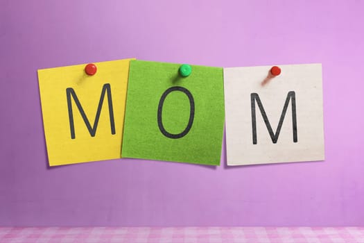 Mom text written on colorful paper note on pink wall background