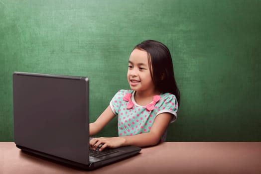 Smiling asian girl using laptop in classroom with chalkboard background