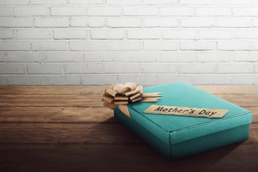 Green gift box with golden ribbon for Mother's Day on wooden table