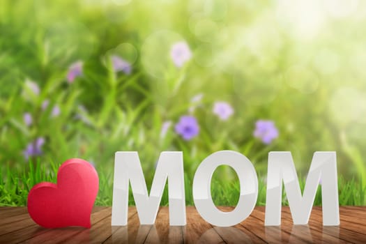 White 3D MOM text with red heart on the wooden table in garden