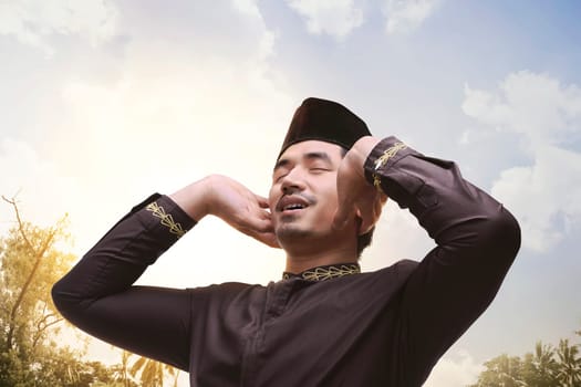 Young asian muslim man with black cap pray at sunset