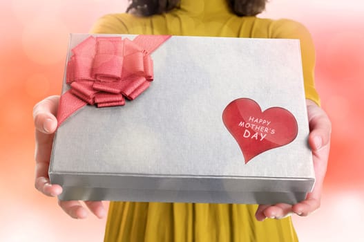 Girl holding a gift box with Happy mothers day message on heart shaped against blurred background