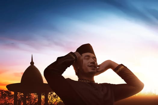 Religious asian muslim man in traditional dress praying to god over sunset background