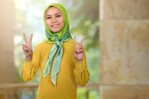 Smiling asian woman girl with hijab showing peace sign in the mosque