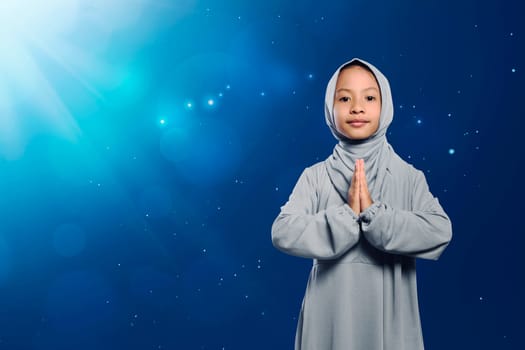 Little asian muslim girl in traditional dress praying against light background