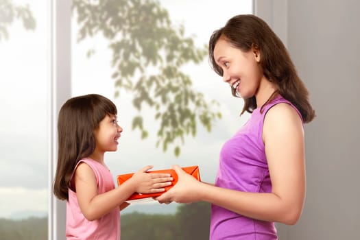 Smiling mother and daughter with gift box in the home. Mothers day concept.