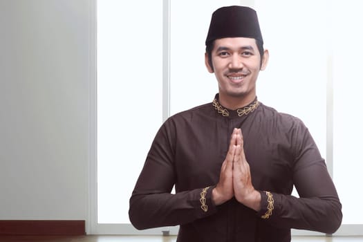Young asian muslim man with black cap praying inside the room