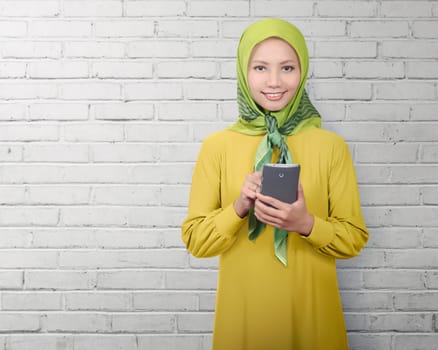 Asian muslim woman standing while using smartphone over white wall background