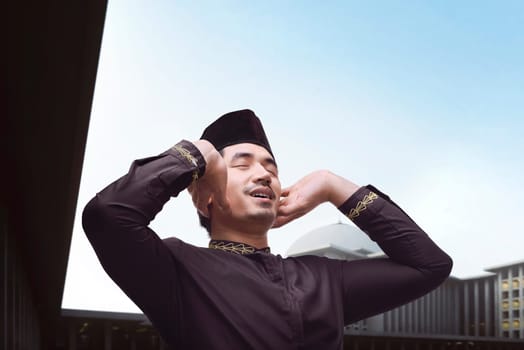 Handsome asian muslim man in traditional dress praying with mosque background