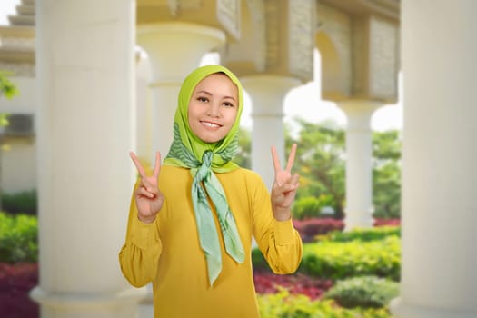Beautiful asian muslim woman showing two fingers over against outdoor background