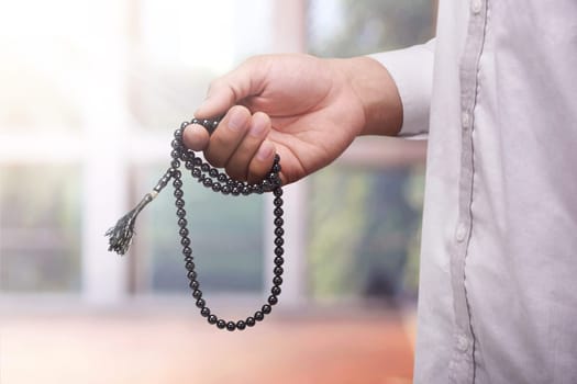 Hand of muslim man praying while holding tasbih against blurred background