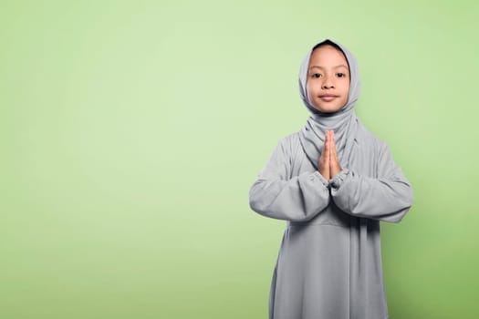 Little asian muslim girl in hijab clothes praying over green background