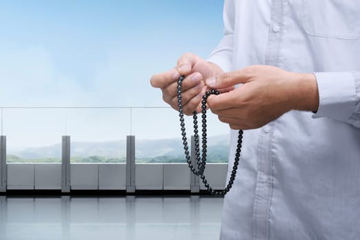 Hands of muslim praying with prayer beads in the balcony against landscape view background