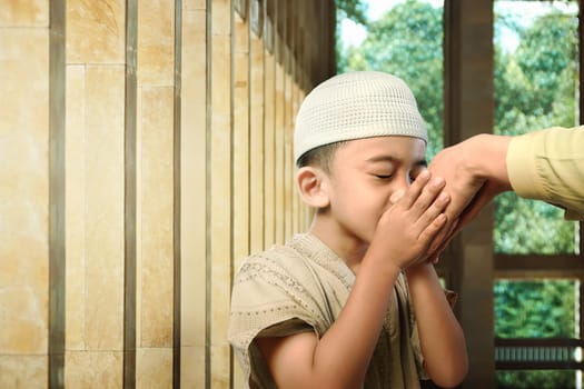 Asian muslim kid kissing his parent hand as respect symbol in the mosque