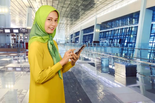 Young asian muslim woman messaging on a smartphone in the airport