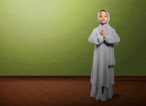 Asian muslim child with veil praying and standing on wooden floor