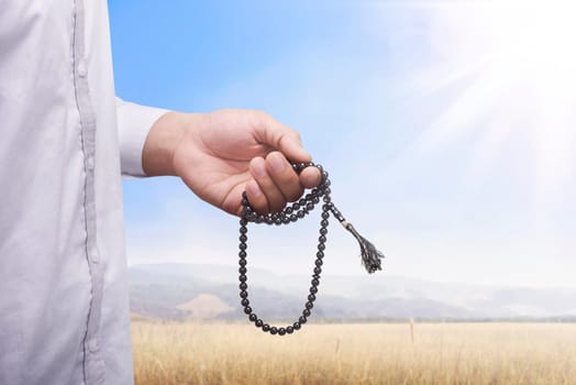 Hand of muslim man praying while holding tasbih with meadow field background