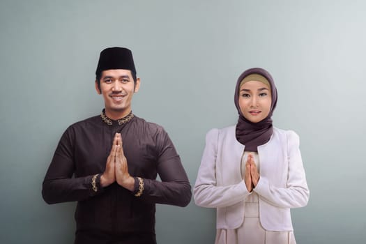 Asian muslim man and woman with traditional dress praying together over grey background