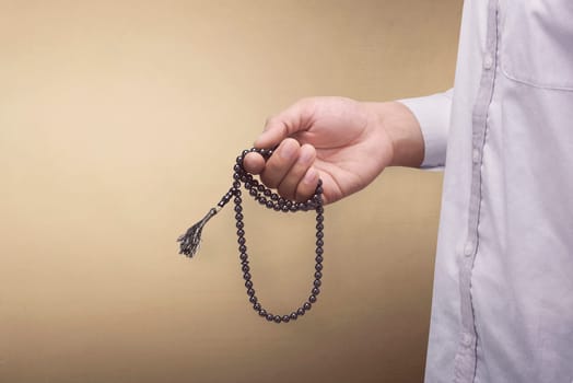 Hand of muslim man praying while holding tasbih over brown background