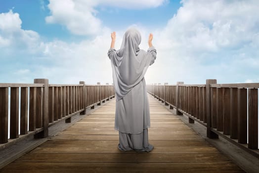 Back view of asian muslim girl standing and praying to god with blue sky background
