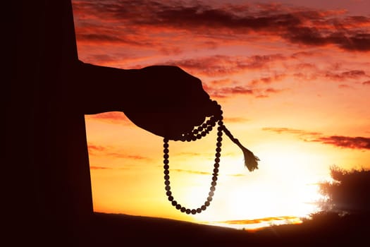 Silhouette of muslim man hand praying while holding tasbih with sunset background